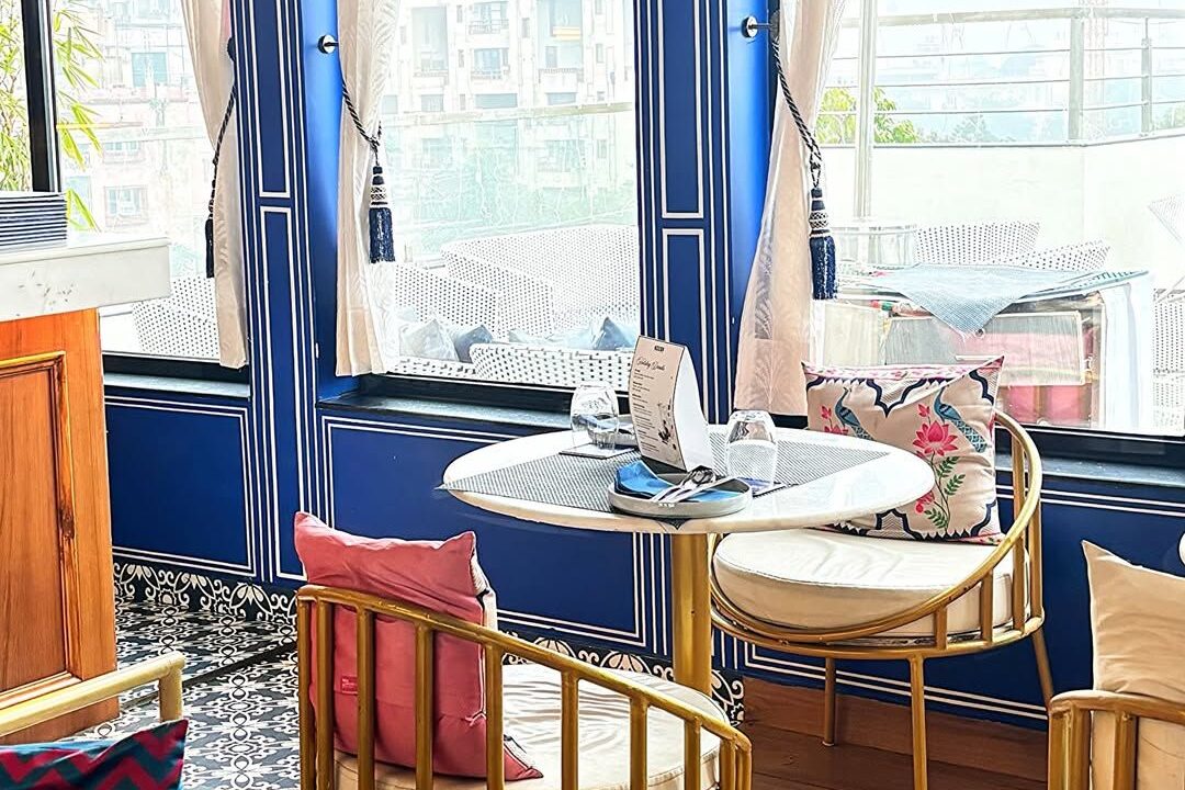 Interior seating with blue chairs beside a window at Nouba Restaurant and Rooftop Lounge, C-Scheme Jaipur
