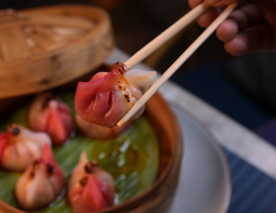 A dumpling in chopsticks over green sauce at Nouba Restaurant and Rooftop Lounge, C-Scheme Jaipur