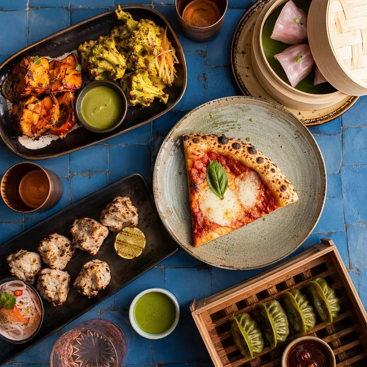 Assorted dishes from three kitchens on a table with Jaipur skyline view at Nouba Restaurant and Rooftop Lounge, C-Scheme Jaipur