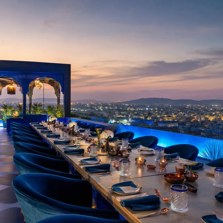 Rooftop dining area with tables set for large group and Jaipur skyline view at Nouba Restaurant and Rooftop Lounge, C-Scheme Jaipur